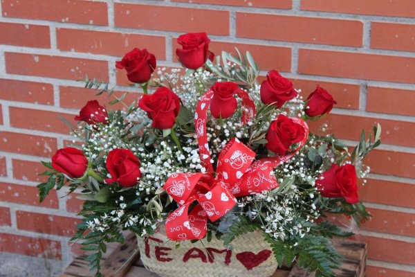 capazo de rafia natural con 12 rosas rojas. En el capazo lleva el texto "te amo" escrito