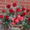 capazo de rafia natural con 12 rosas rojas. En el capazo lleva el texto "te amo" escrito